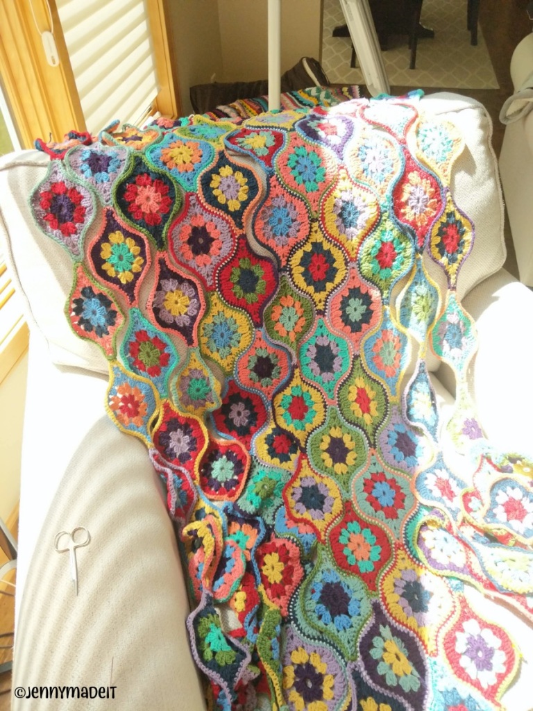 This is a photo of a crochet blanket in many bright colors that is nearly finished. 
