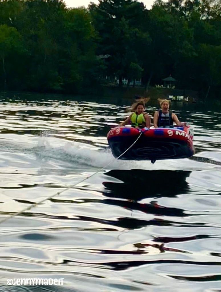This is a photo of myself and a friend on a raft being towed by a boat on a lake. We are airborne above the water while looking frightened.